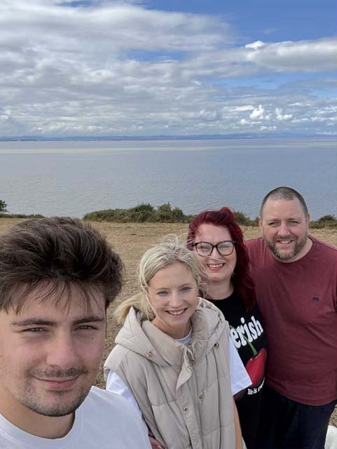 two men and two men take a selfie with a beach and the sea behind them