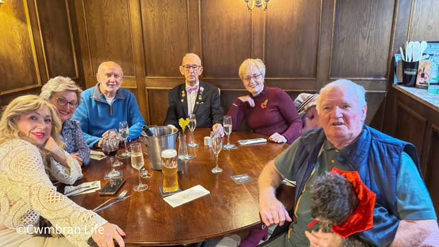 six people sat at a pub table smile for the camera