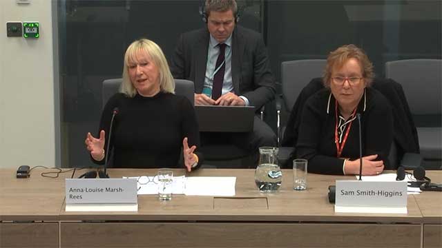 two women sat at wooden desk with papers in front of them