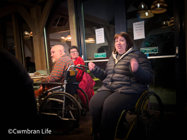 a woman in a wheelchair talking to a room of people