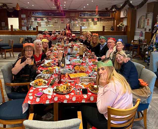 a large group of men, women and children at a Christmas day table ready for dinner