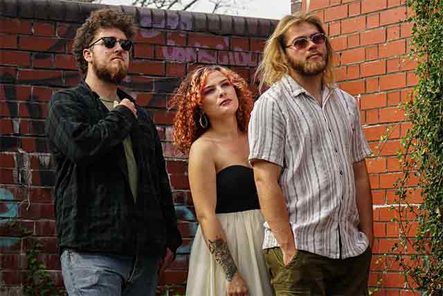 three members of band stood by wall