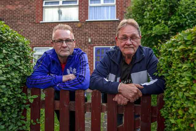 two men lean over a garden fence