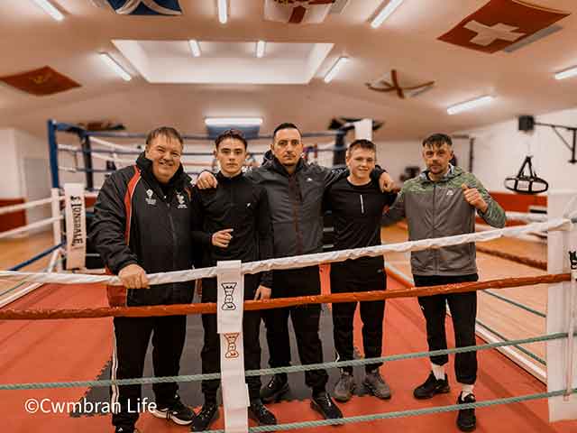 two teenage boys and three men in a boxing ring