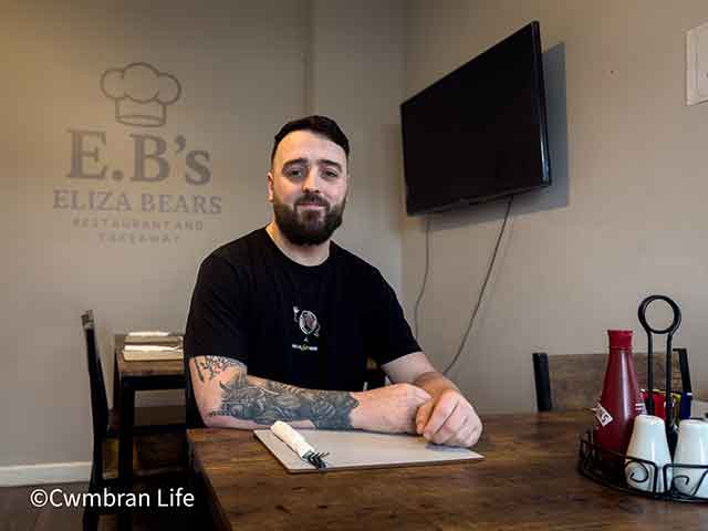 a man at a table in cafe- on the wall it says EBs (eliza bears) restaurant and takeaway