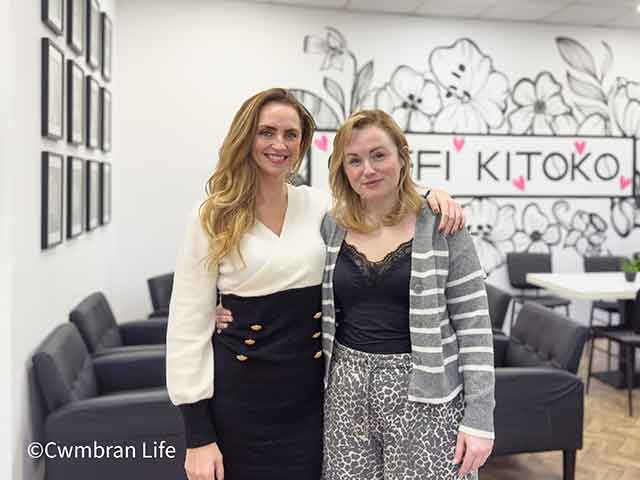 two women stood in a cafe- with the work 'kitoko' on the wall- the cafe is called 'Coffi Kitoko'