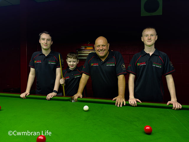 three boys and a man lean on a snooker table