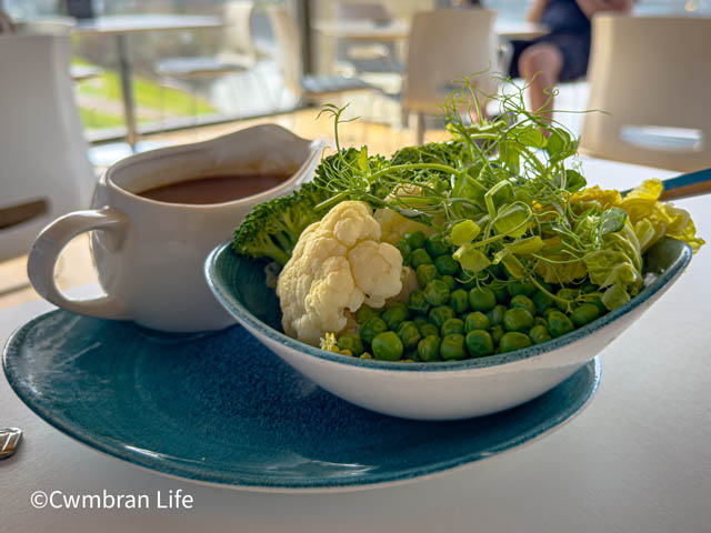 a bowl of green peas and cauliflower next to a gravy jug