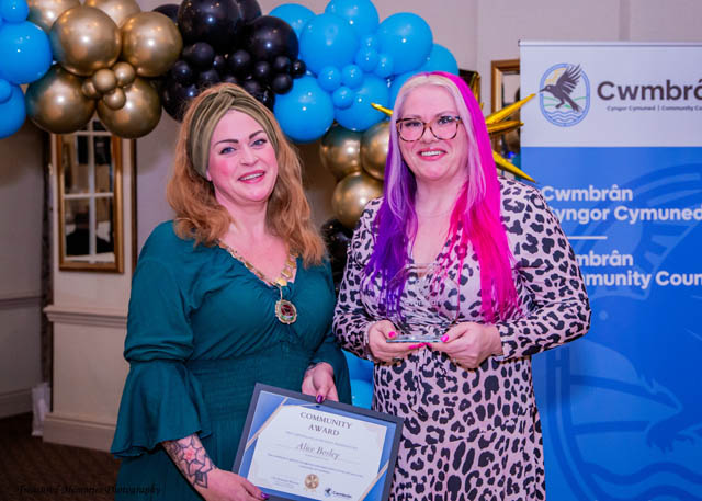two women hold a certificate in front of a balloon arch