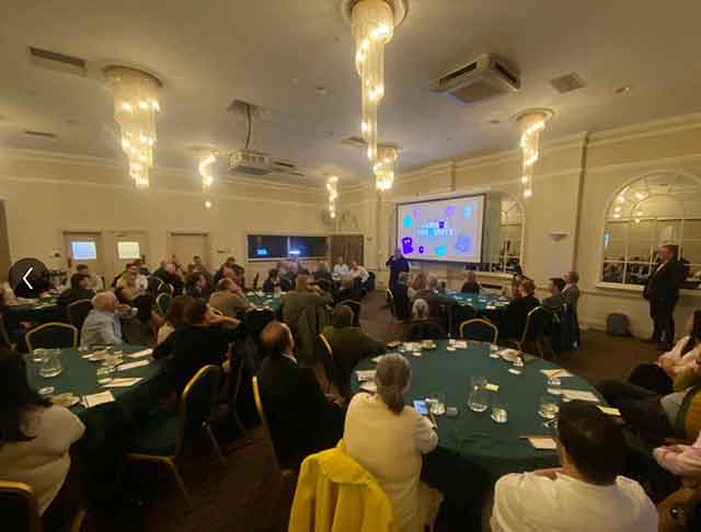 a room full of people sat at tables watching a man speak to them