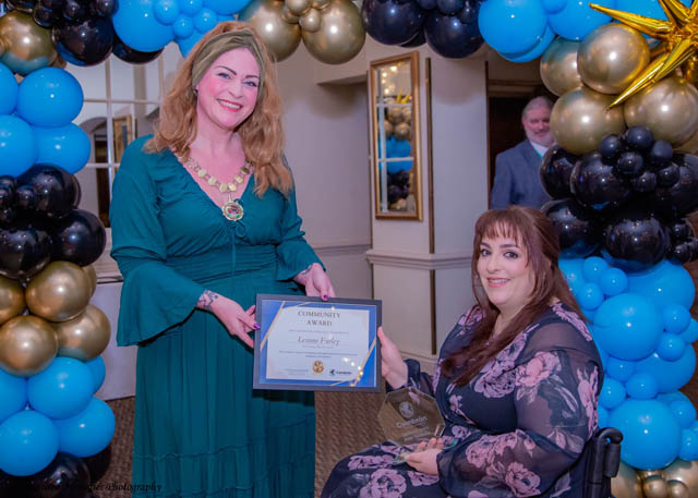 two women, one in a wheelchair, hold a certificate