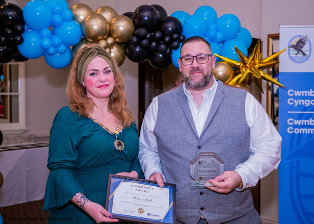 a man and a woman hold a certificate in front of a balloon arch