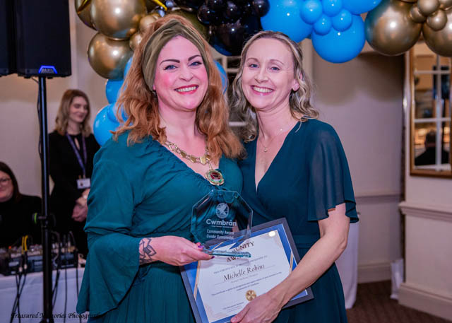 two women hold a certificate in front of a balloon arch