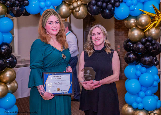 two women hold a certificate in front of a balloon arch