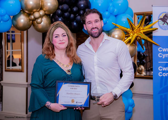 a man and a woman hold a certificate in front of a balloon arch
