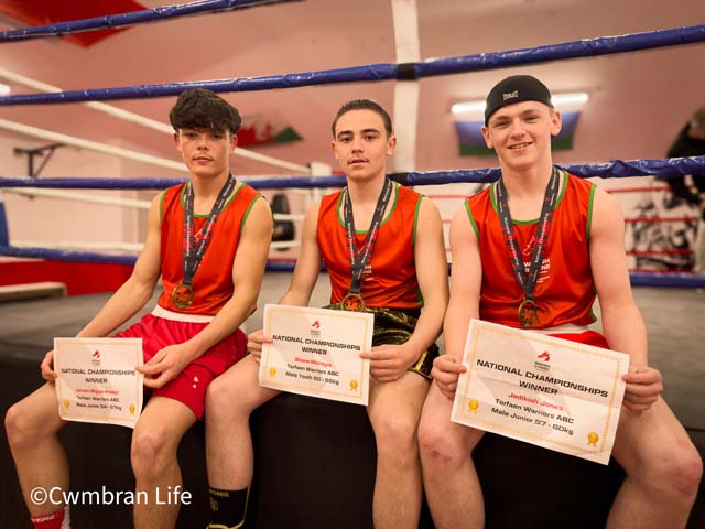 three teenage boys sat on edge of a boxing ring