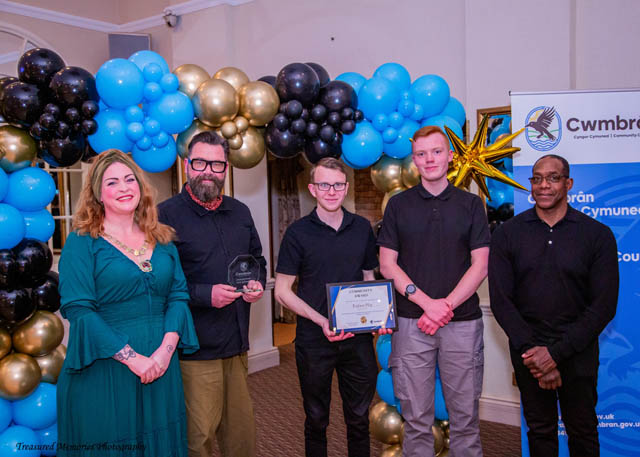 a group of five people stood by a balloon arch with a certificate