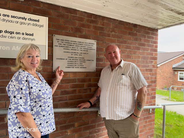 a man and woman stood by a plaque about a 50th anniversary of a housing scheme
