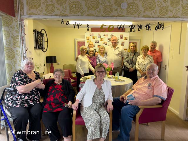 a group of people in a lounge by a 50th birthday banner