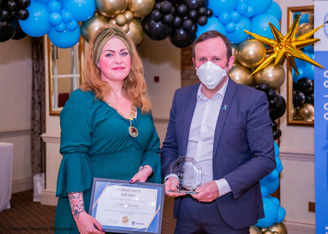 a man and a woman hold a certificate in front of a balloon arch