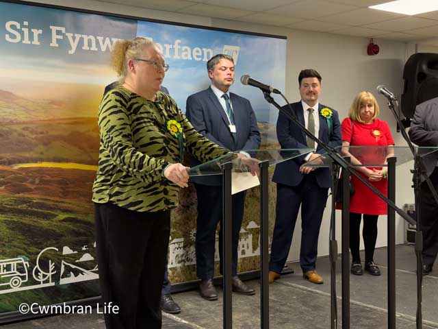 a woman gives a speech at a lecturn with three people in the background