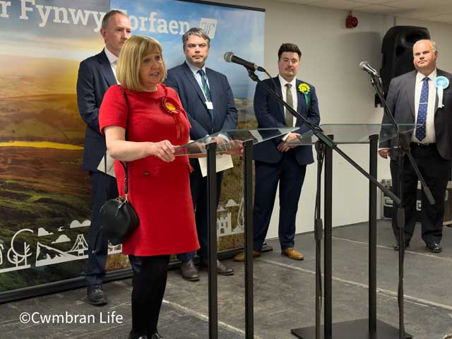 a woman gives a speech at a lecturn with four people in the background
