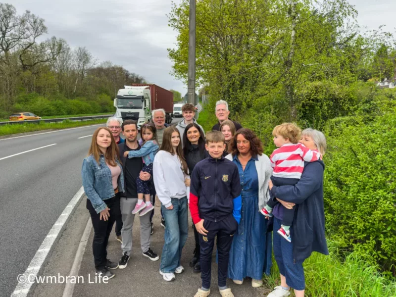 a group of residents by a busy road with a lorry driving past