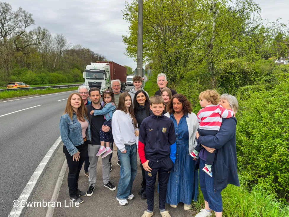 a group of residents by a busy road with a lorry driving past