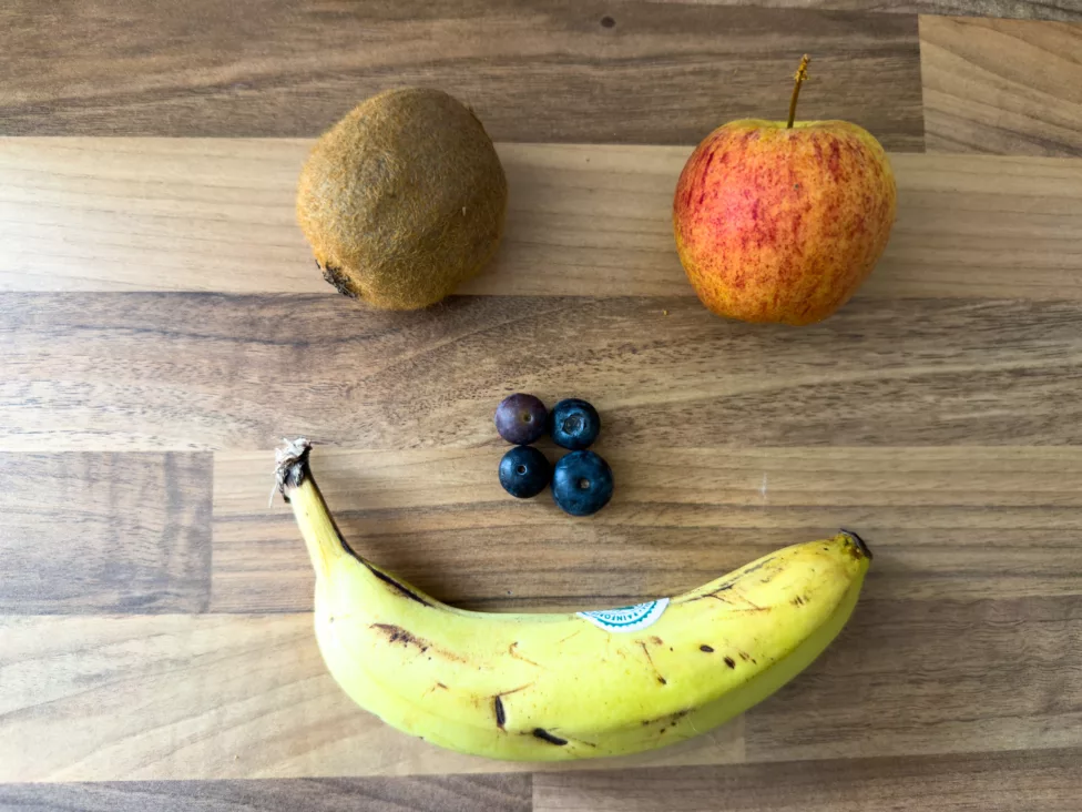 a banana, blueberries, apple and kiwi fruit in the shape of a smiling face