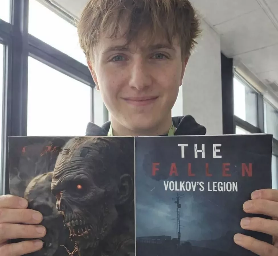 a man holding up a book called - The Fallen