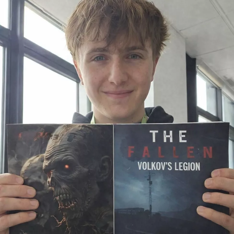 a man holding up a book called - The Fallen