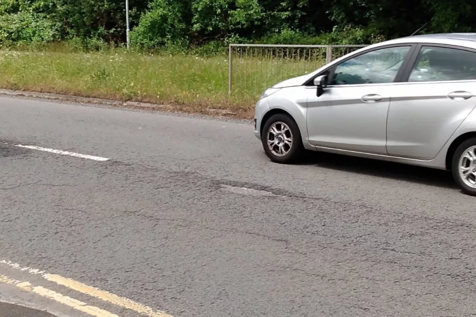 A car passing a pothole on the road.