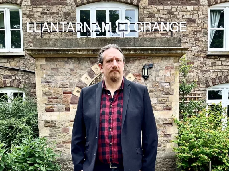 a man in front of a building with a sign llantarnam grange above it