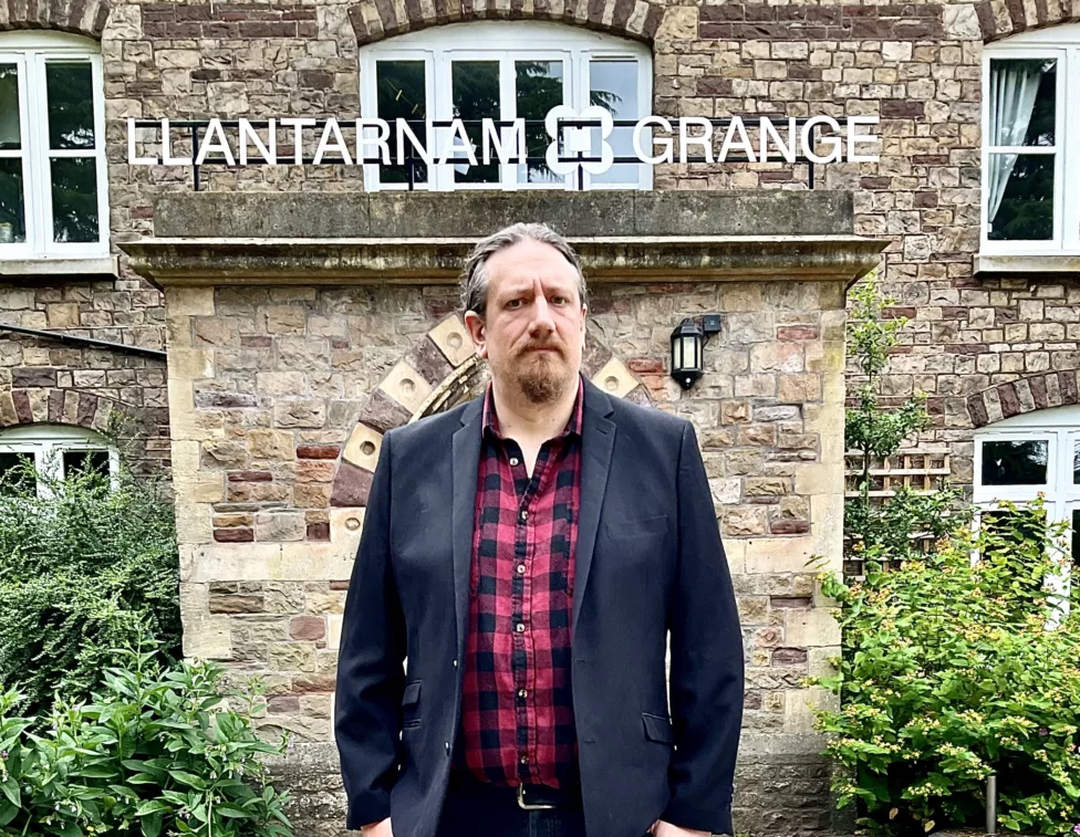 a man in front of a building with a sign llantarnam grange above it