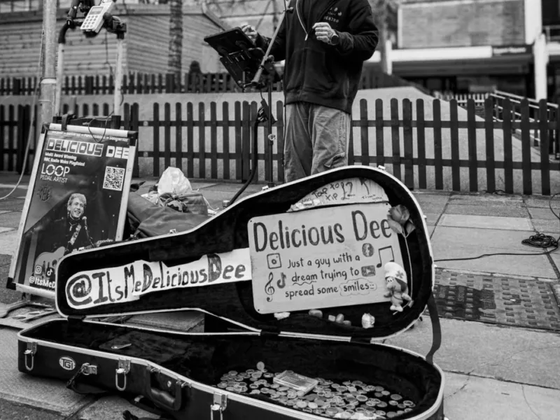 a black and white photo of a man singing and playing a guitar - he's busking in a town centre