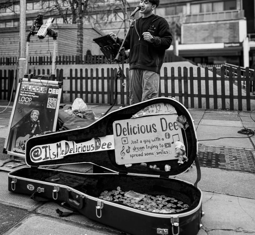a black and white photo of a man singing and playing a guitar - he's busking in a town centre