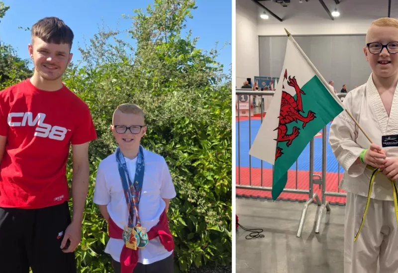 a photo of a nine year old boy holding a wales flag dressed in a white martial arts outfit- and stood with a teenage boy wearing medal