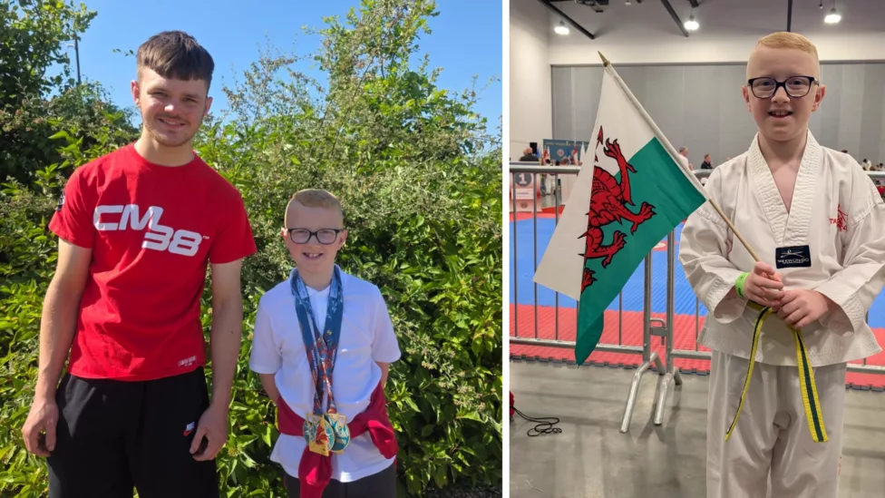 a photo of a nine year old boy holding a wales flag dressed in a white martial arts outfit- and stood with a teenage boy wearing medal