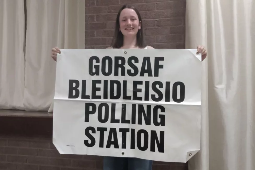 a teenage girl holding a banner saying 'polling station'