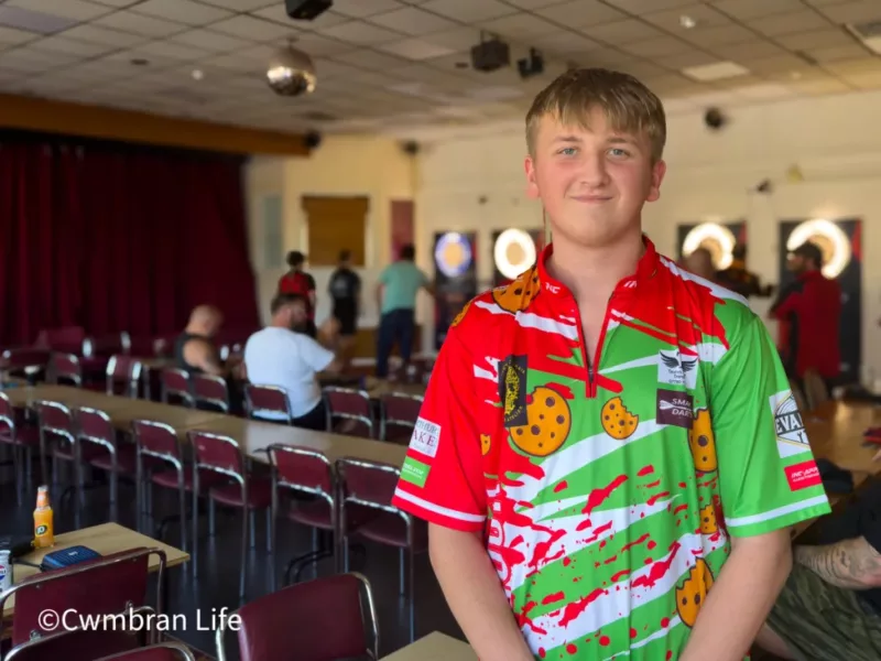 a teenage boy in a room in front of people playing darts