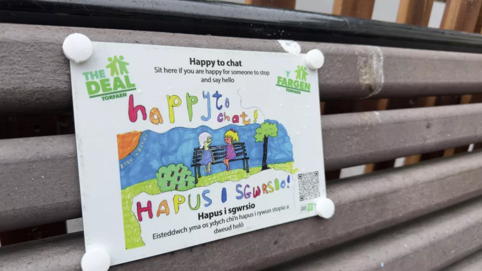 a plaque saying 'happy to chat' on a wooden bench