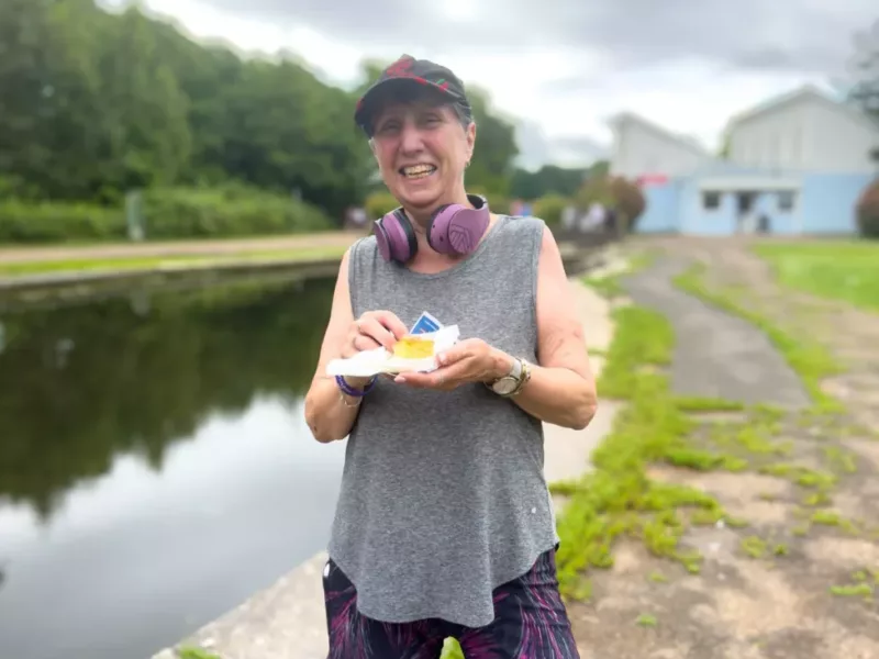 a woman in running clothes eating a cake by a pond