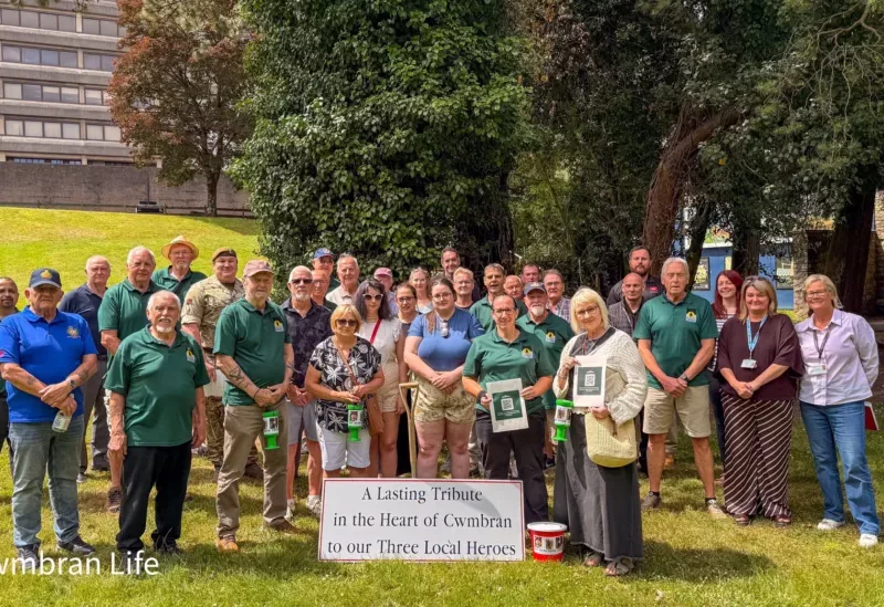a group of people stood on a grassed area next to card saying 'lasting tribute in the heart of cwmbran to our local heroes'