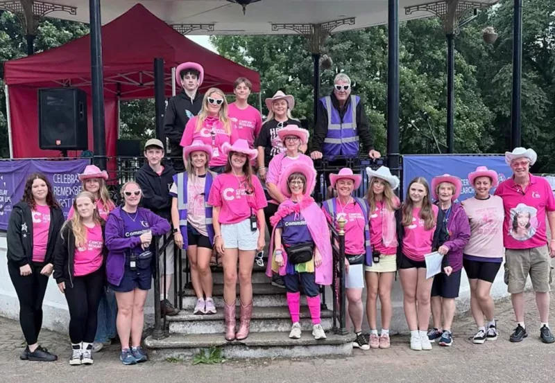 a team of men and women- many in pink clothes stood by a bandstand