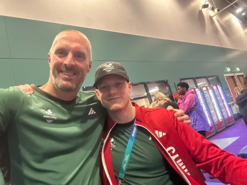 two men arm in arm smile at the camera