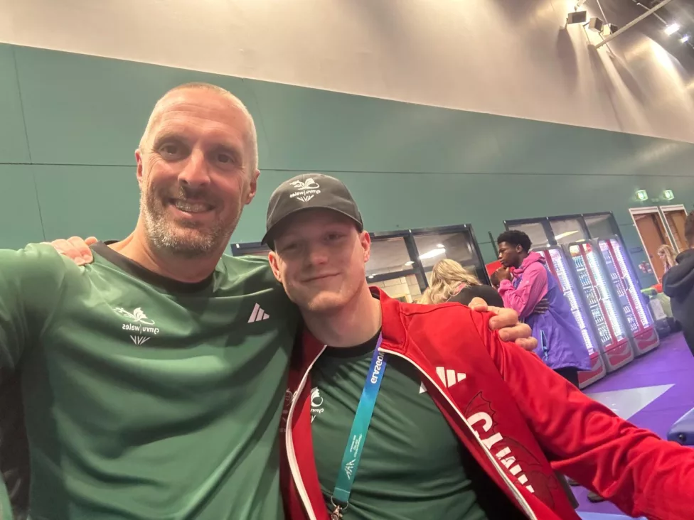 two men arm in arm smile at the camera