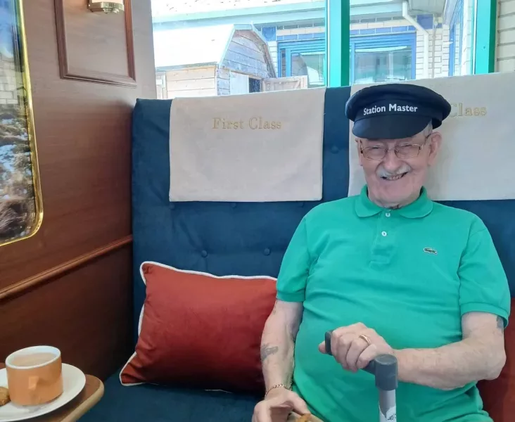 a photo of an older man in a train conductor hat sat in a train seat