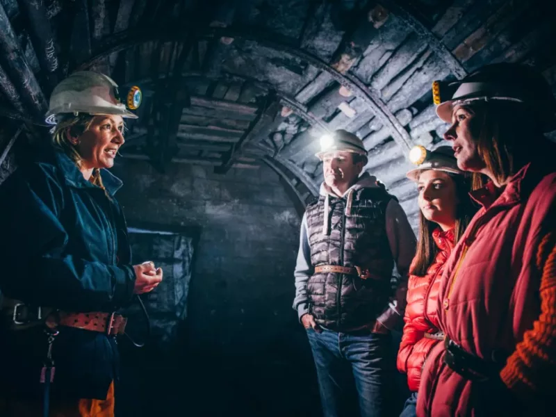 a family in a mine wearing head lamps listing to a guide