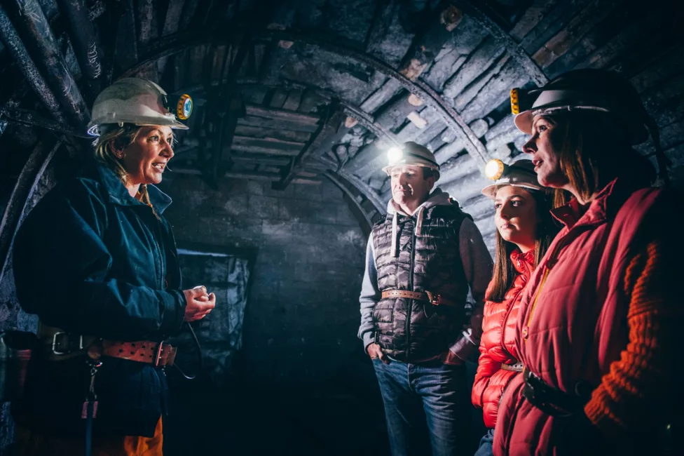 a family in a mine wearing head lamps listing to a guide