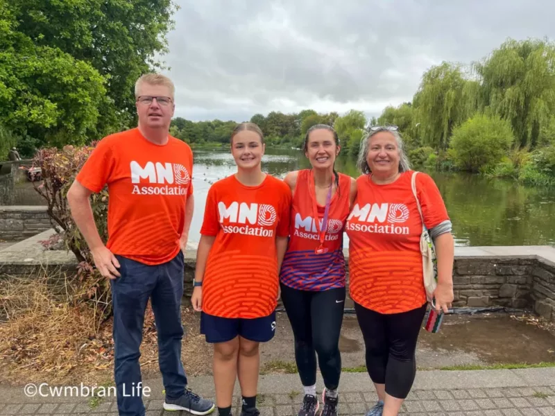three women and man stand in orange t-shirts with MND association on by a lake